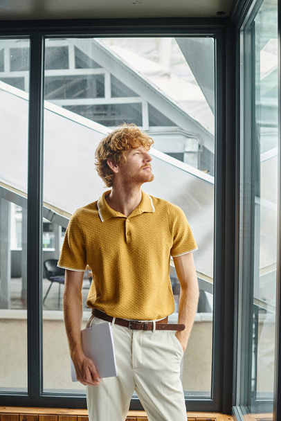 mladý rudovlasý muž v elegantní ležérní žluté košili odvrací pohled s okenní pozadí, spolupráce - Fotografie, Obrázek