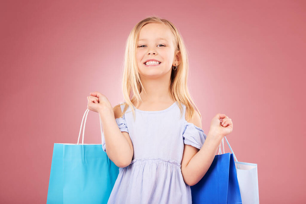 Portrait, happy and girl kid with shopping bag, customer and purchase with fashion isolated on pink background. Retail, smile and young child with gift, luxury and buying, discount and sale in studio. - Photo, Image