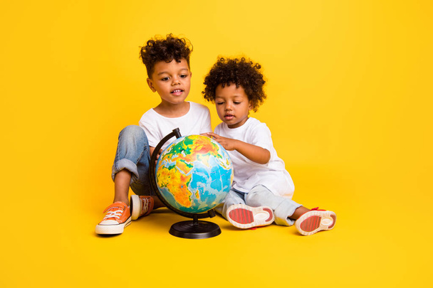 Full body portrait of cute intelligent curious brothers sit floor look planet earth globe isolated on yellow color background. - Valokuva, kuva