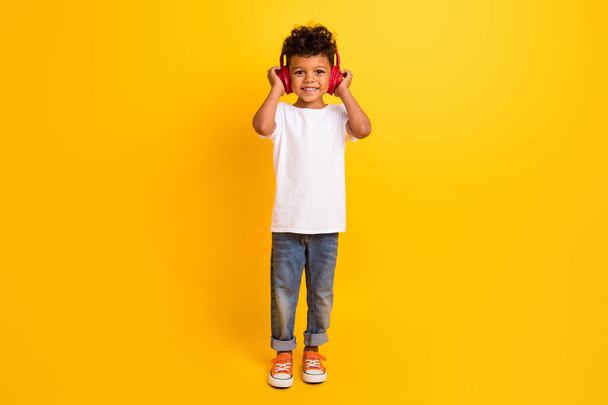 Pełna długość zdjęcie pozytywne wesoły mały chłopiec nosić biały t-shirt słuchanie muzyki słuchawki izolowane żółty kolor tło. - Zdjęcie, obraz