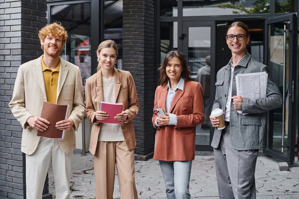 equipo creativo joven posando afuera sonriendo ante la cámara sosteniendo papeles, teléfono y taza de café, coworking - Foto, imagen
