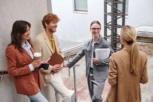 vier collega 's in smart attires genieten van lunchpauze buiten lachen en chatten, coworking - Foto, afbeelding