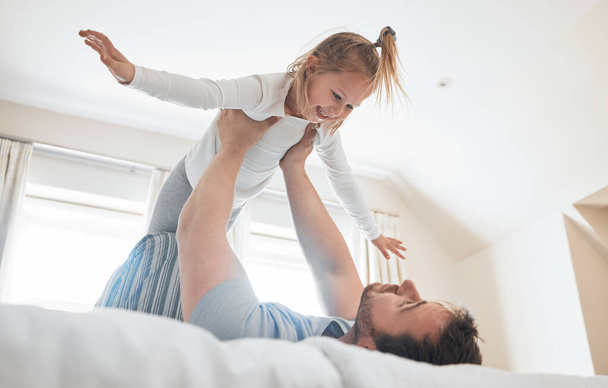 Girl, father and happy on bed for airplane games, energy and relax for crazy fun at home. Dad, child and excited to fly in bedroom for freedom, fantasy and lift to balance for play, trust and support. - Photo, Image