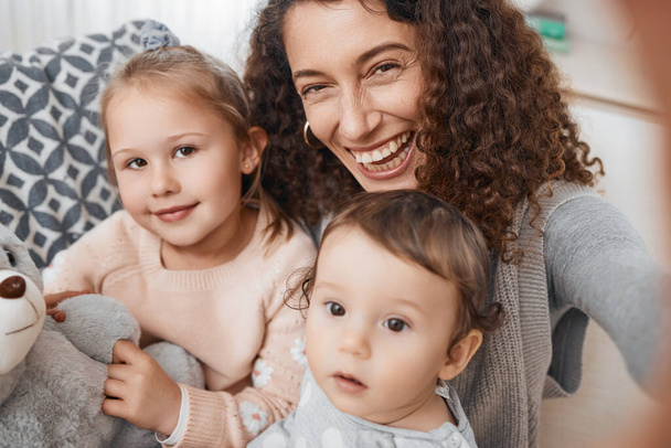 Selfie, smile and portrait of mother with her children bonding, relaxing and playing in the living room. Happy, love and young mom taking a picture with her kids for memory together in lounge at home. - Foto, imagen
