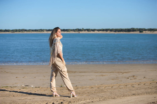 Mooie jonge blonde vrouw loopt op het zand van het strand aan de zuidkust van spanje in Sanlucar de barrameda, stad van wijn en gastronomie, op de achtergrond riviermonding en nationaal park. - Foto, afbeelding