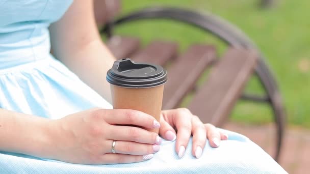 Ein Mädchen im blauen Kleid trinkt im Park Kaffee. Basteltasse mit Kaffee in den Händen einer Frau in Großaufnahme. Schnappen Sie sich einen Kaffee zum Mitnehmen. Erfrischendes Getränk - Filmmaterial, Video