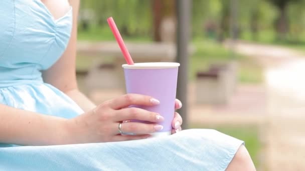 Tyttö sinisessä mekossa juo limonadia puistossa. Kupillinen laventeli väri käsissä naisen lähikuva. Ota ryyppy mukaan. Virkistävä juoma - Materiaali, video