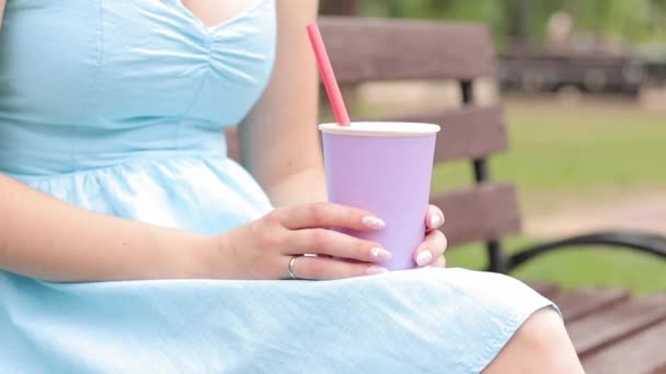 Dziewczyna w niebieskiej sukience pije lemoniadę w parku. Filiżanka koloru lawendy w rękach kobiety z bliska. Napij się na wynos. Napoje orzeźwiające - Materiał filmowy, wideo
