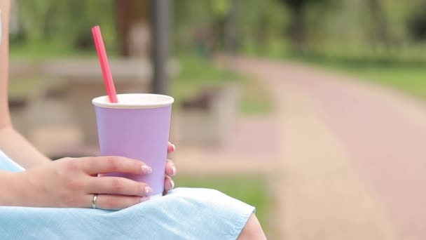 Een meisje in een blauwe jurk drinkt limonade in het park. Een kopje lavendelkleur in de handen van een vrouw van dichtbij. Neem een drankje om mee te nemen. Verfrissend drankje - Video