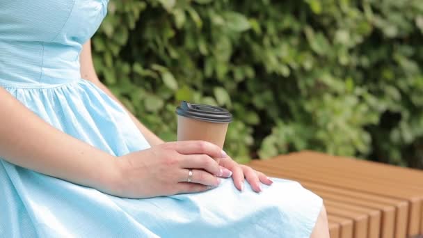 Uma rapariga de vestido azul bebe café no parque. Copo de artesanato com café nas mãos de uma mulher close-up. Traz um café. Bebida revigorante - Filmagem, Vídeo
