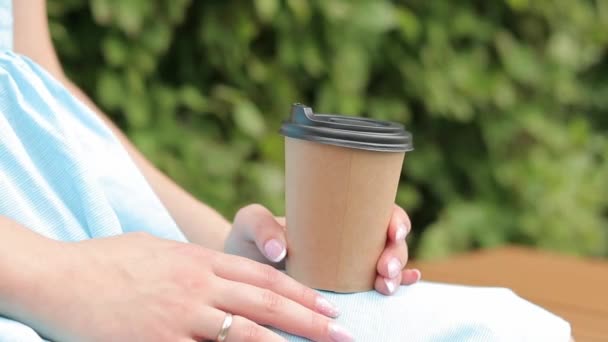A girl in a blue dress drinks coffee in the park. Craft cup with coffee in the hands of a woman close-up. Grab takeaway coffee. Invigorating drink - Footage, Video