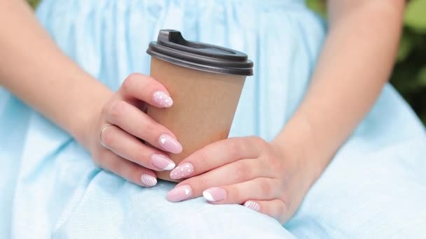 Ένα κορίτσι με μπλε φόρεμα πίνει καφέ στο πάρκο. Κούπα με καφέ στα χέρια μιας γυναίκας από κοντά. Πάρε καφέ απ 'έξω. Αναζωογονητικό ποτό - Πλάνα, βίντεο