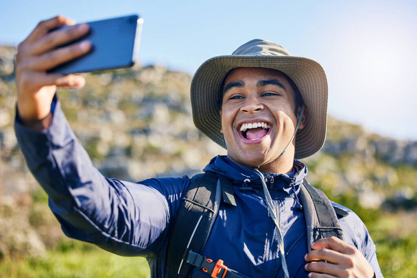 Selfie, wolność i człowiek wędrujący latem po górach w poszukiwaniu podróży, przygód lub eksploracji. Natura, uśmiech i fotografia ze szczęśliwym młodym turystą robiącym zdjęcie profilowe na zewnątrz w słońcu. - Zdjęcie, obraz