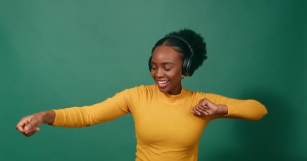 Молода чорна жінка танцює з навушниками, зелений студійний фон. Високоякісні 4k кадри - Кадри, відео