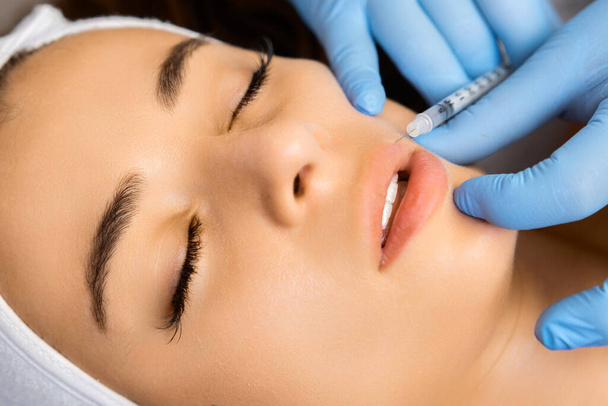 Молода красива жінка отримує ін'єкцію ботоксу в губи для збільшення губ косметологом в салоні краси  - Фото, зображення