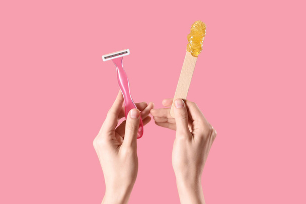 Mains tenant la spatule avec de la pâte à sucre et un rasoir sur fond rose. Concept d'épilation - Photo, image
