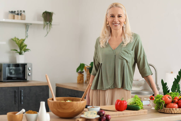 Donna matura che fa insalata di verdure a tavola in cucina - Foto, immagini