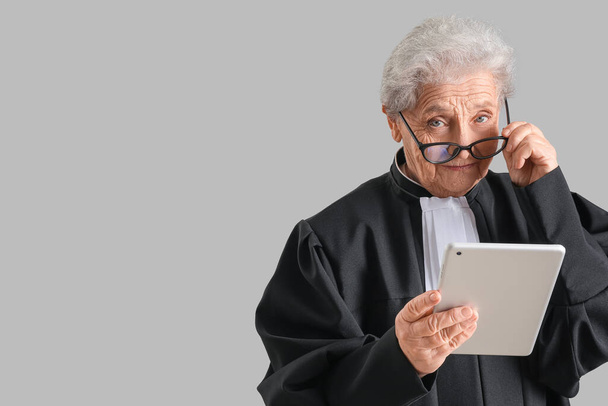 Giudice anziano con tablet su sfondo grigio - Foto, immagini