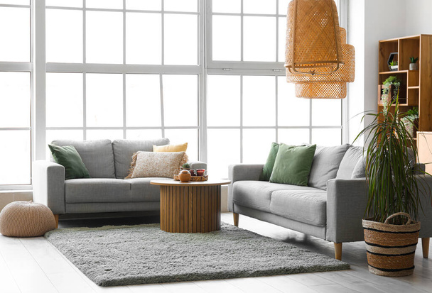 Інтер'єр світлої вітальні з затишними сірими диванами і журнальним столиком на м'якому килимку - Фото, зображення