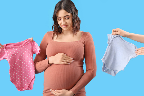 Junge schwangere Frau und weibliche Hände mit Babybody auf blauem Hintergrund - Foto, Bild