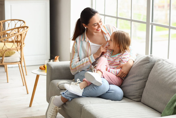 Bambina con sua madre seduta sul divano di casa - Foto, immagini