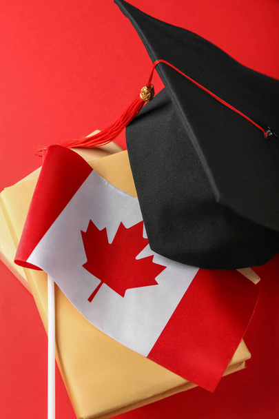 Σημαία του Καναδά με καπέλο αποφοίτησης και βιβλία σε κόκκινο φόντο - Φωτογραφία, εικόνα