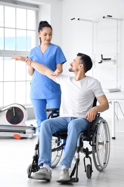 Physiotherapeutin arbeitet mit jungem Mann im Rollstuhl im Reha-Zentrum - Foto, Bild