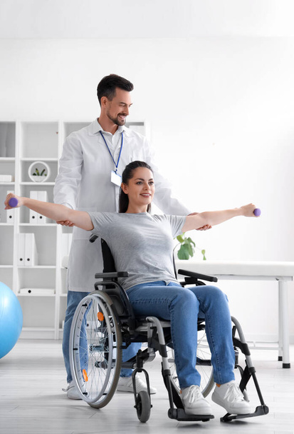 Männlicher Physiotherapeut arbeitet mit junger Frau im Rollstuhl im Reha-Zentrum - Foto, Bild