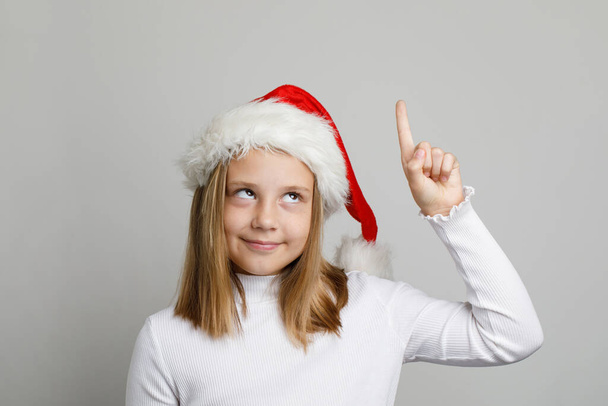 Natale ritratto di divertente bambina in cappello di Babbo Natale che punta su sfondo bianco - Foto, immagini