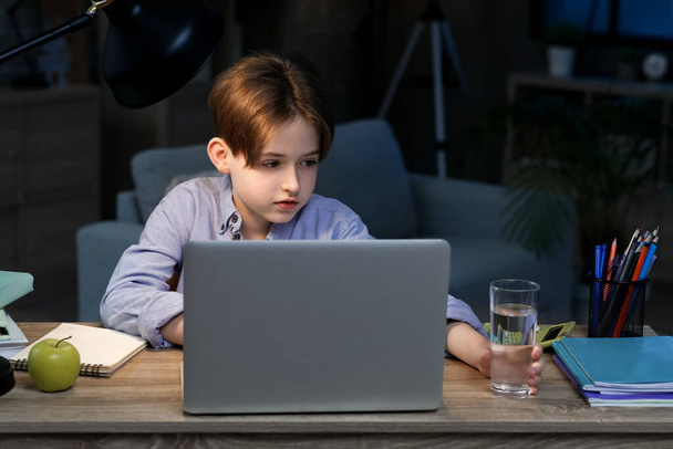 Niño haciendo la tarea con el ordenador portátil y tomando un vaso de agua en casa tarde en la noche - Foto, imagen