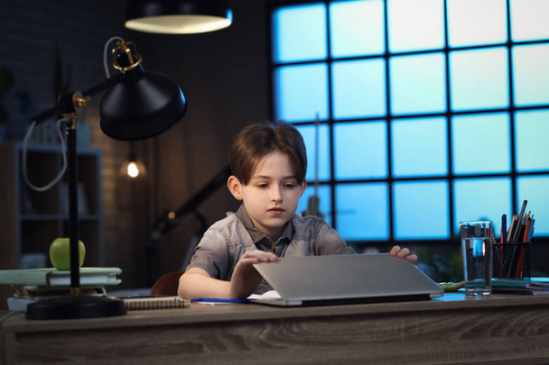 Мальчик делает домашнюю работу с ноутбуком дома поздно вечером - Фото, изображение