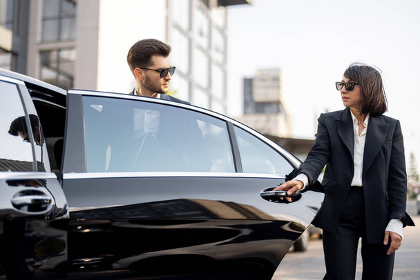 Vrouwelijke chauffeur helpt een zakenman om uit de auto te stappen. Een deur openen. Begrip persoonlijke chauffeur, luxe taxi of zakenreis - Foto, afbeelding