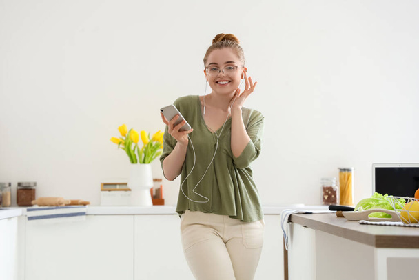 Mujer joven y feliz escuchando música y bailando en la cocina ligera - Foto, Imagen