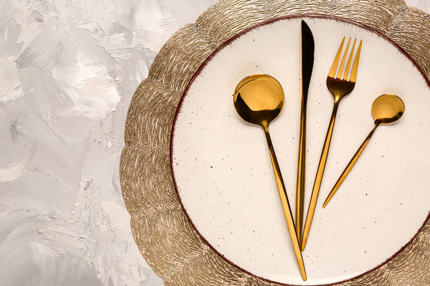 Coloque esteira com prato limpo e conjunto de talheres dourados na mesa grunge cinza - Foto, Imagem