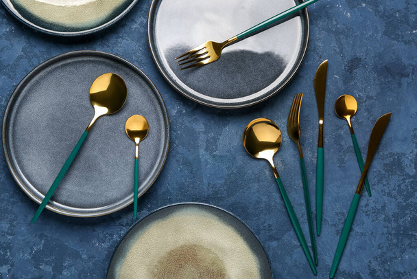 Tischdekoration mit sauberen Tellern und goldenem Besteck auf blauem Grunge-Hintergrund - Foto, Bild