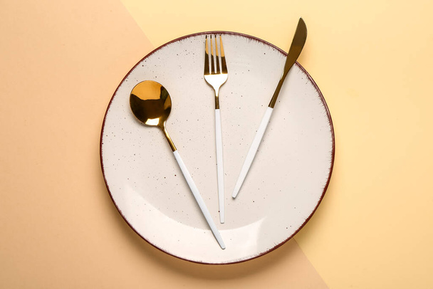 Чистая тарелка с набором золотых столовых приборов на бежевом фоне, крупным планом - Фото, изображение