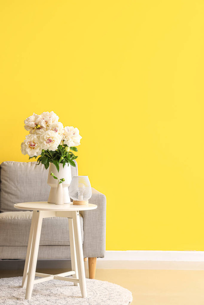 Jarrón de peonías blancas con mesa de centro y sofá cerca de la pared amarilla - Foto, imagen