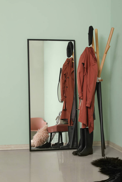 Καθρέπτης και σχάρα με ρούχα κοντά σε πράσινο τοίχο στο διάδρομο - Φωτογραφία, εικόνα
