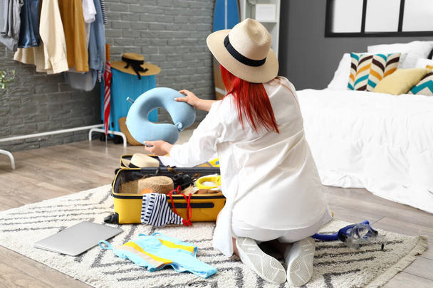 Junge Frau mit Nackenkissen packt Koffer im Schlafzimmer aus - Foto, Bild