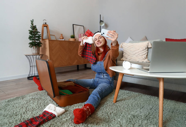 Молодая женщина с рождественским носком делает селфи дома - Фото, изображение