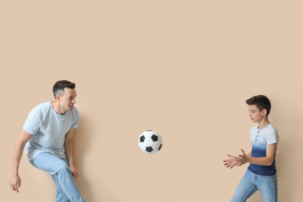 Little boy with his dad playing football on beige background - Photo, Image