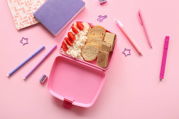 Обеденный стол с вкусной едой и различными канцелярскими принадлежностями на розовом фоне - Фото, изображение