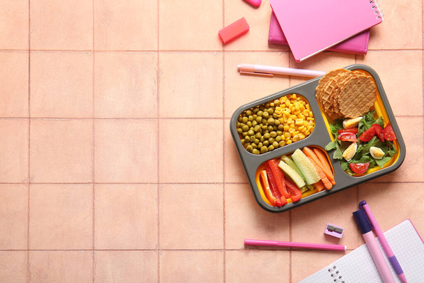 Ланчбокс с вкусной едой и различными канцелярскими принадлежностями на фоне апельсиновой плитки - Фото, изображение