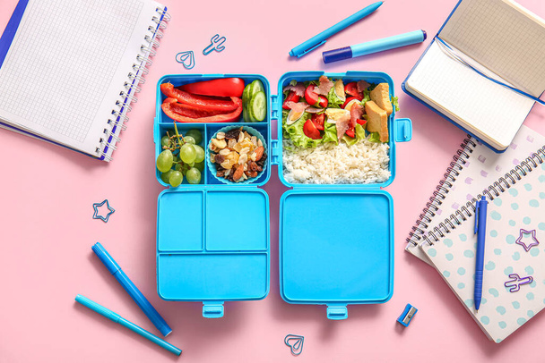 Обідня коробка з смачною їжею та різними канцтоварами на рожевому фоні - Фото, зображення