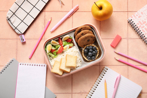 Lunchbox με νόστιμο φαγητό και διάφορα χαρτικά σε πορτοκαλί φόντο πλακιδίων - Φωτογραφία, εικόνα