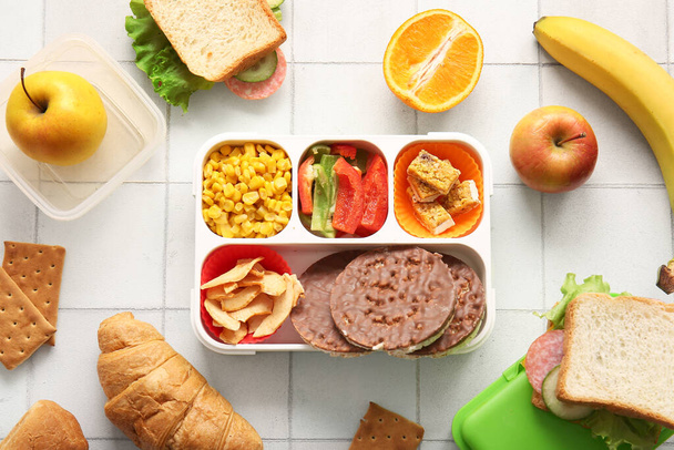 Обідні коробки з різною смачною їжею на фоні білої плитки - Фото, зображення
