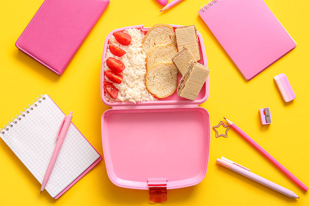Lunchbox με νόστιμο φαγητό και διάφορα χαρτικά σε κίτρινο φόντο - Φωτογραφία, εικόνα
