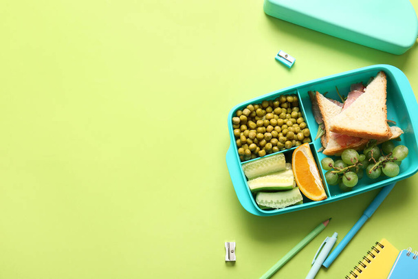 Scatola da pranzo con cibo delizioso e articoli di cancelleria diversi su sfondo verde - Foto, immagini