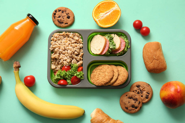 Lunchbox avec une délicieuse nourriture et une bouteille de jus sur fond turquoise - Photo, image