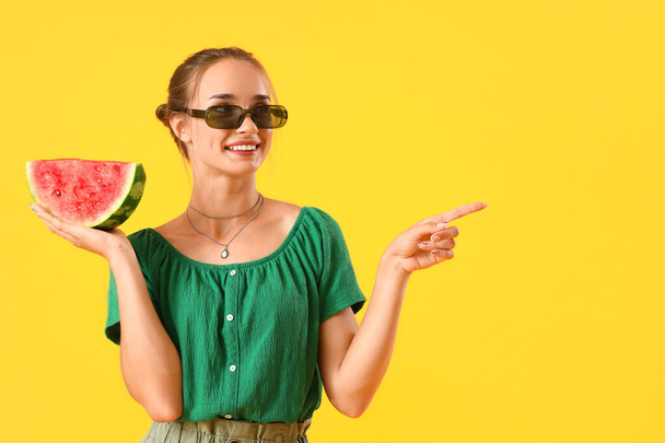 Junge Frau mit frischer Wassermelone zeigt auf etwas auf gelbem Hintergrund - Foto, Bild